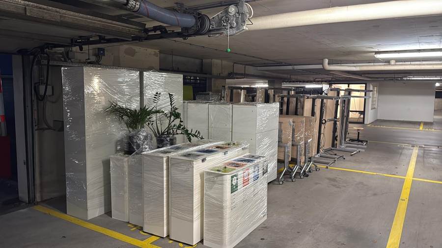 Wrapped office cabinets, desks and plants staged in a parking garage after unloading